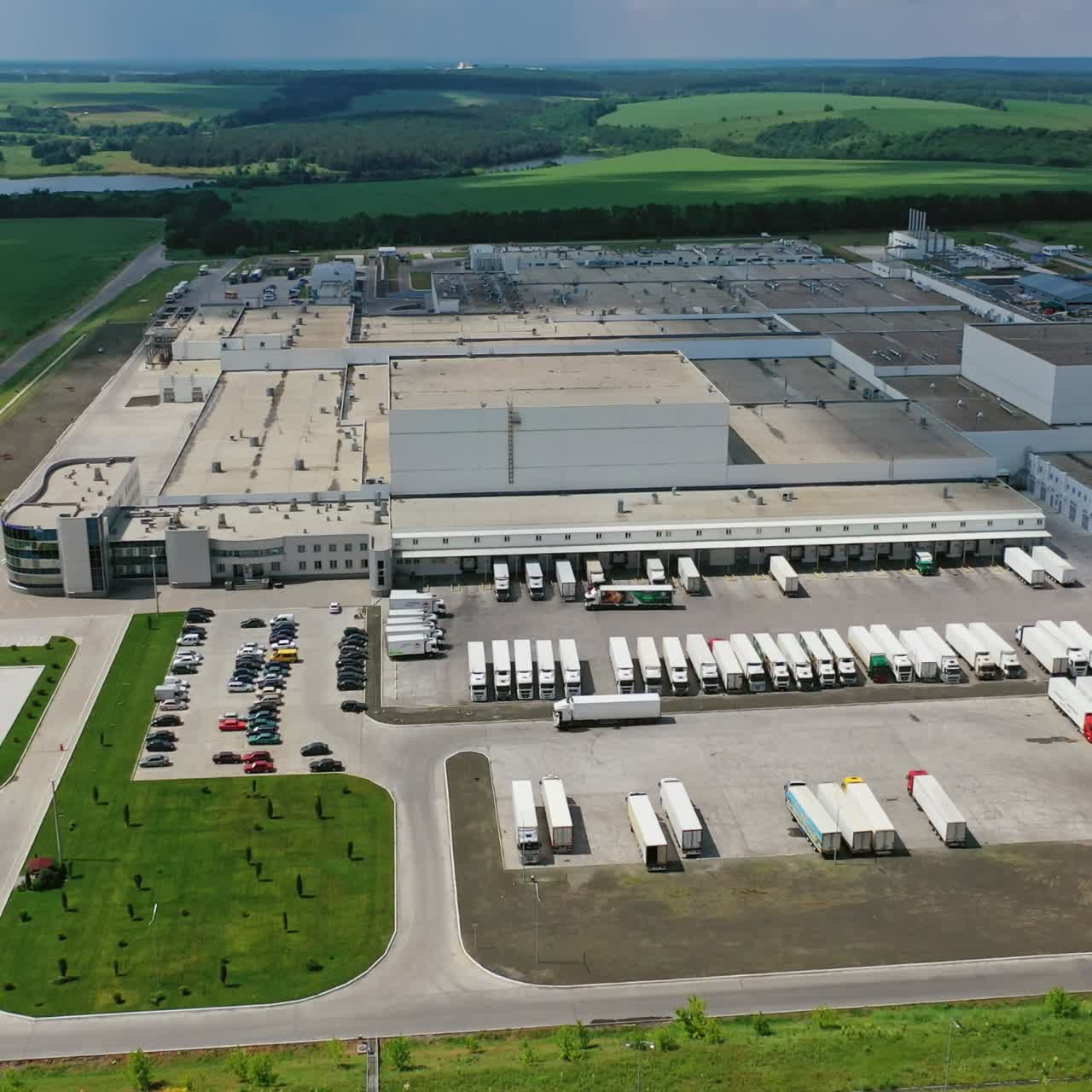 Industrial plant on nature background. Large territory of industry with parking for trucks. Modern factory on field. Aerial view.