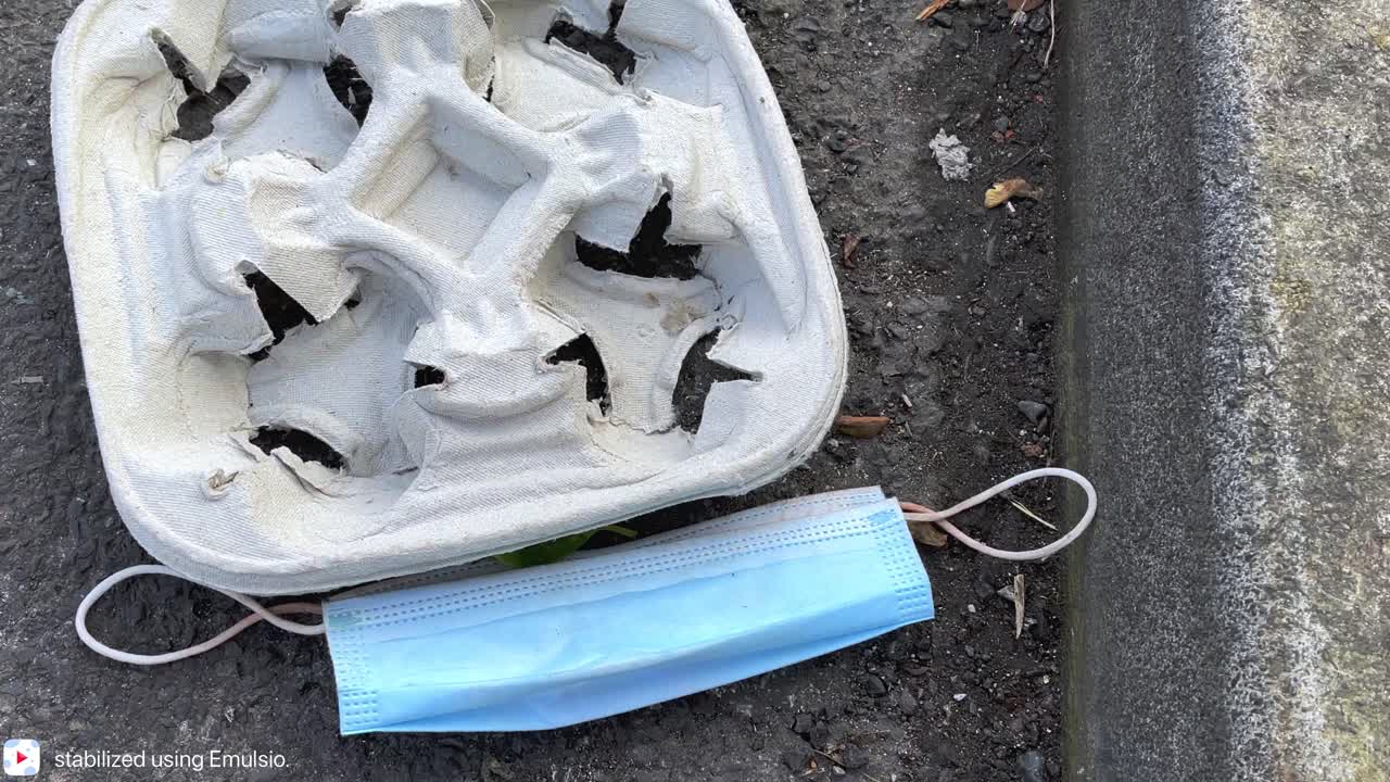 Medical grade face mask abandoned in the street next to a 4 cup holder, pandemic waste, biohazard waste. 4K 60ffs