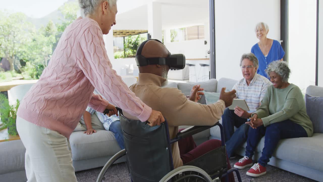 Anziani felici di diverse etnie, incluso un uomo in sedia a rotelle, che utilizzano visori VR in una casa di riposo.