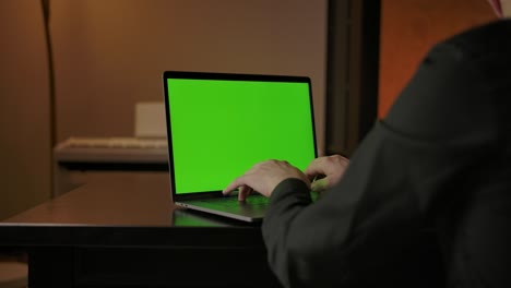 hombre escribiendo en el teclado de la computadora portátil con pantalla verde, dolly fuera disparo deslizante suave
