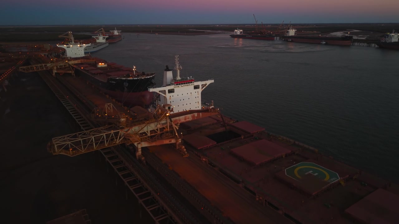 Aerial of raw materials being loaded onto a ship in Port Hedland Australia at sunset