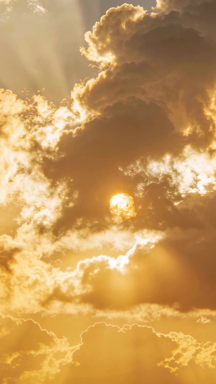 Vertical video: Sun sinking behind central cloud at sunset, opening lower gap, revealing sunbeams