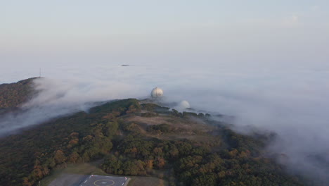 Heavy-dense-cloud-of-fog-covering-the-hill-with-several-structures-on-it-in-the-evening