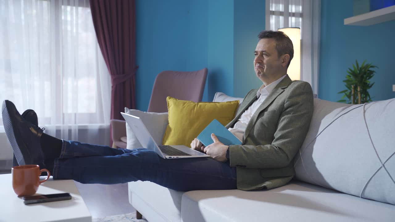 Mature man working at home relaxed and carefree, working on laptop on sofa, taking notes.