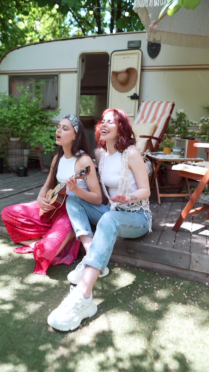 dos amigos tocando el ukulele al aire libre cerca de una caravana