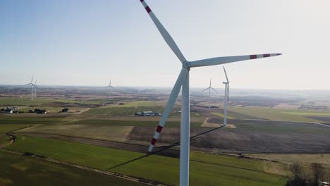 Große-Windkraftanlagen-Mit-Rotorblättern-Im-Feld,-Luftaufnahme,-Leuchtend-Orangefarbener-Sonnenuntergang,-Blauer-Himmel,-Windpark,-Zeitlupe,-Drohnendrehung