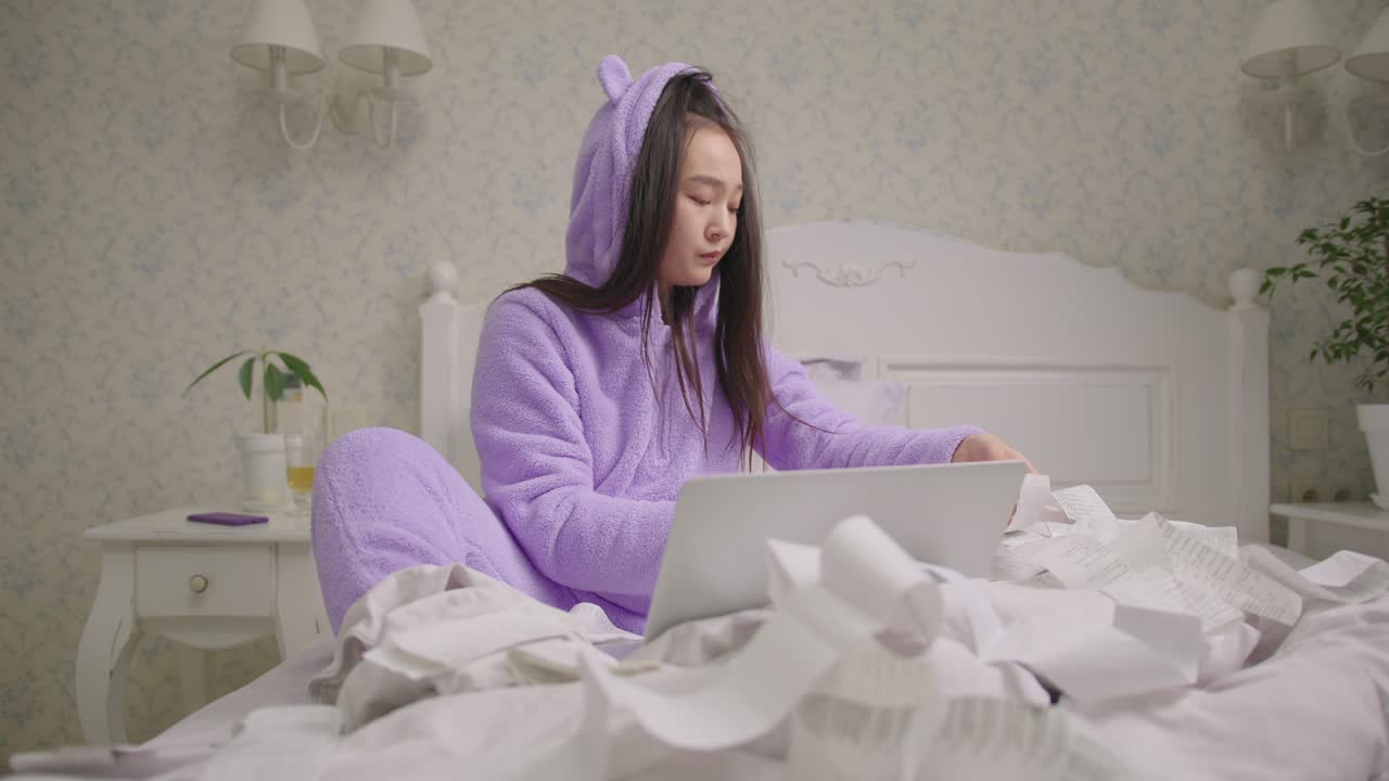 20대 아시아 여성이 침대에 앉아 큰 상점 영수증을 확인하고 있습니다. 수천 년 된 사람이 수입과 지출을 계산하고 있습니다.