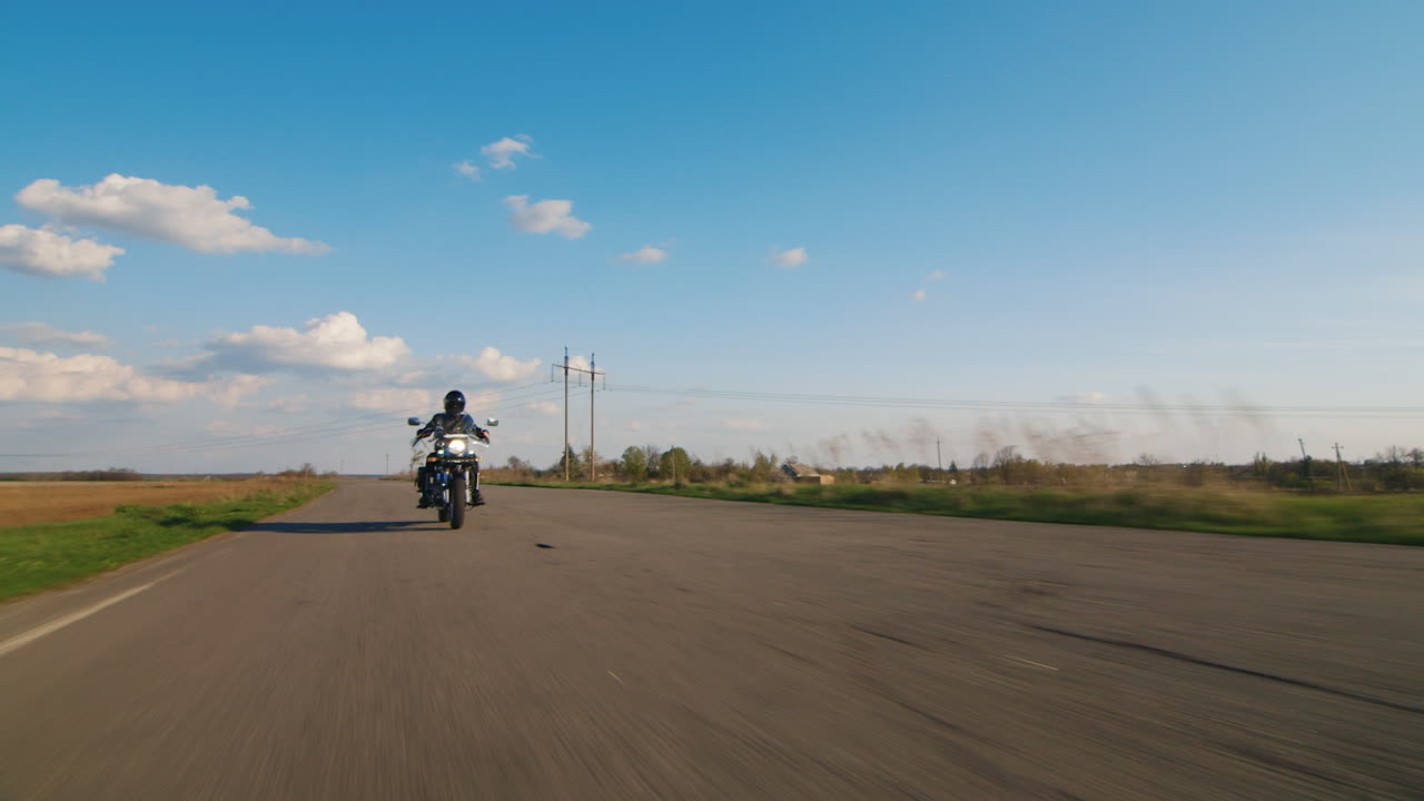 Un motociclista solitario che guida su una strada deserta. Grandangolo.