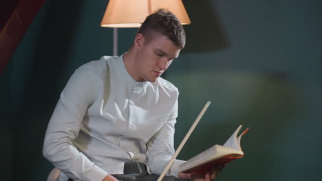 close-up of player in white shirt reading book while holding cue stick with serious focus. intense expression reflects deep concentration. warm lighting adds depth to strategic atmosphere