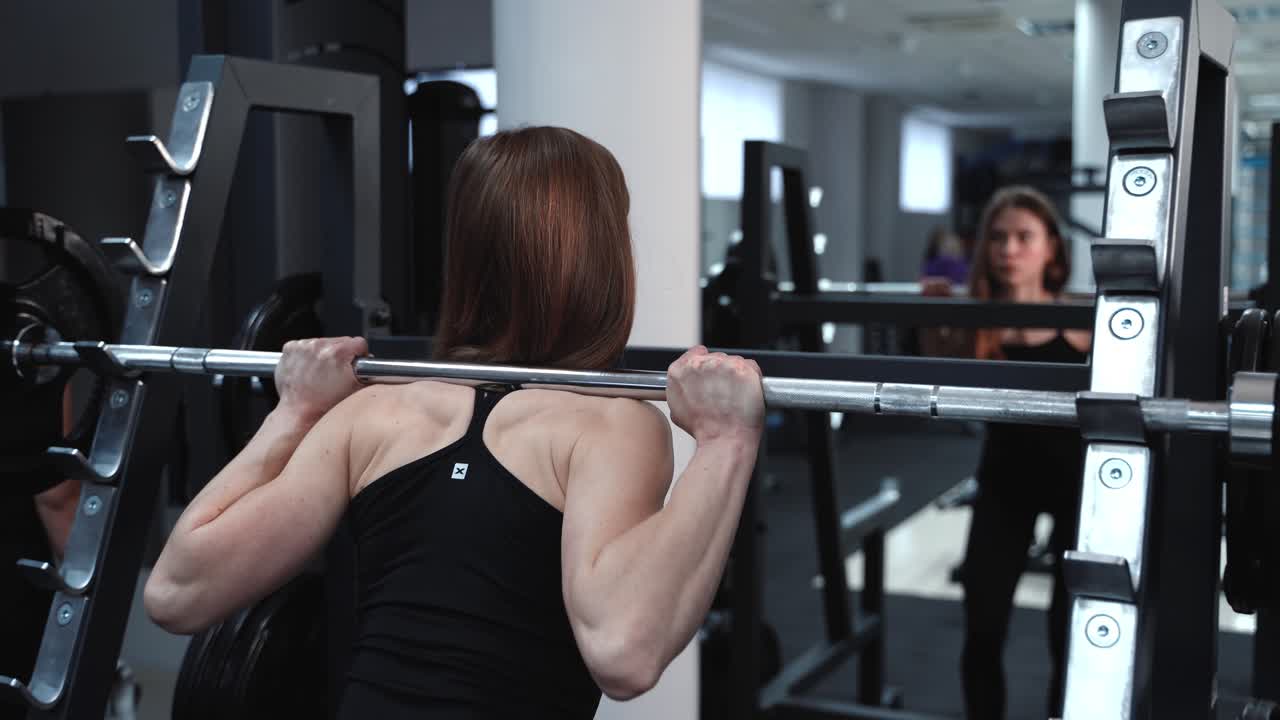 Athletic young woman walks up to the weight bar and lifts her in the fitness club opposite the mirror. Endurance exercise