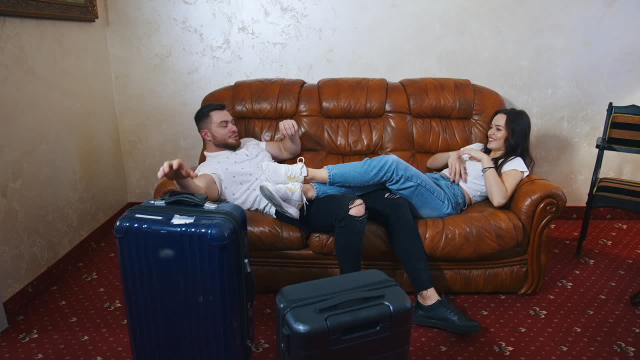 Young just married couple having fun laying on couch in hotel room. Man and woman has just arrived on vocation.
