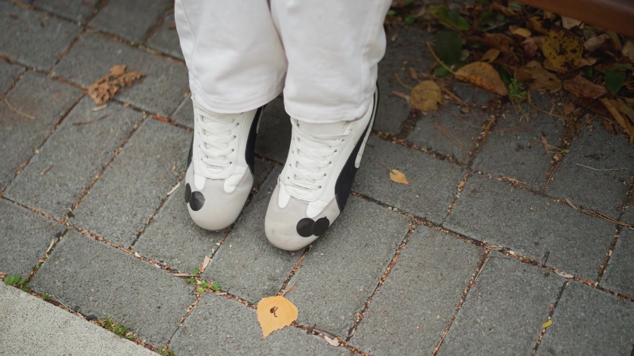 Närbild på flicka i vita sneakers med svarta detaljer och lösa byxor som utför rytmiska fotrörelser på grå tegelbeläggning beströdd med fallna löv. fokus förblir konsekvent