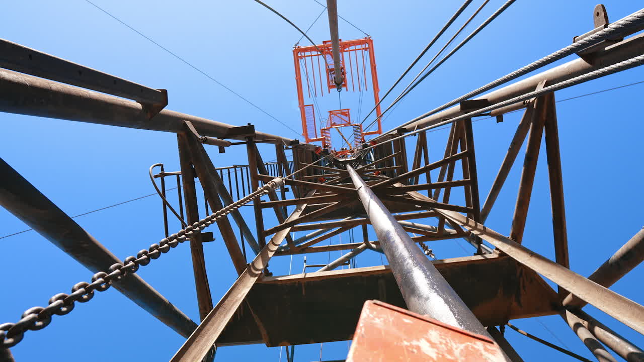 High metal tower with used at the site for drilling mineral natural resources. Low angle view on the support for oil production.
