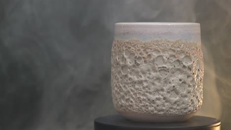 dolly rechts von einem keramikglas mit korallen-textur, das sich um seine achse in den gelben rauch dreht