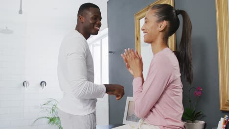 Video-of-happy-diverse-couple-relaxing-at-home,-laughing-and-having-fun-with-water-in-bathroom