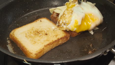 Gooey-soft-egg-stacked-onto-thick-fried-breakfast-sandwich-in-skillet