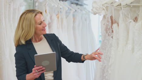 mature female owner of bridal wedding dress shop with digital tablet