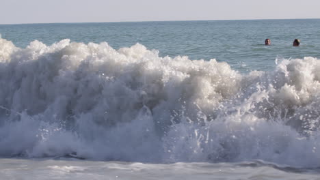 waves crashing on beach with people swimming