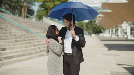 Happy-young-muslim-couple-hiding-from-sun-under-umbrella.