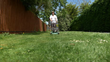 low, wide angle, slider shot of man mowing garden on a sunny day