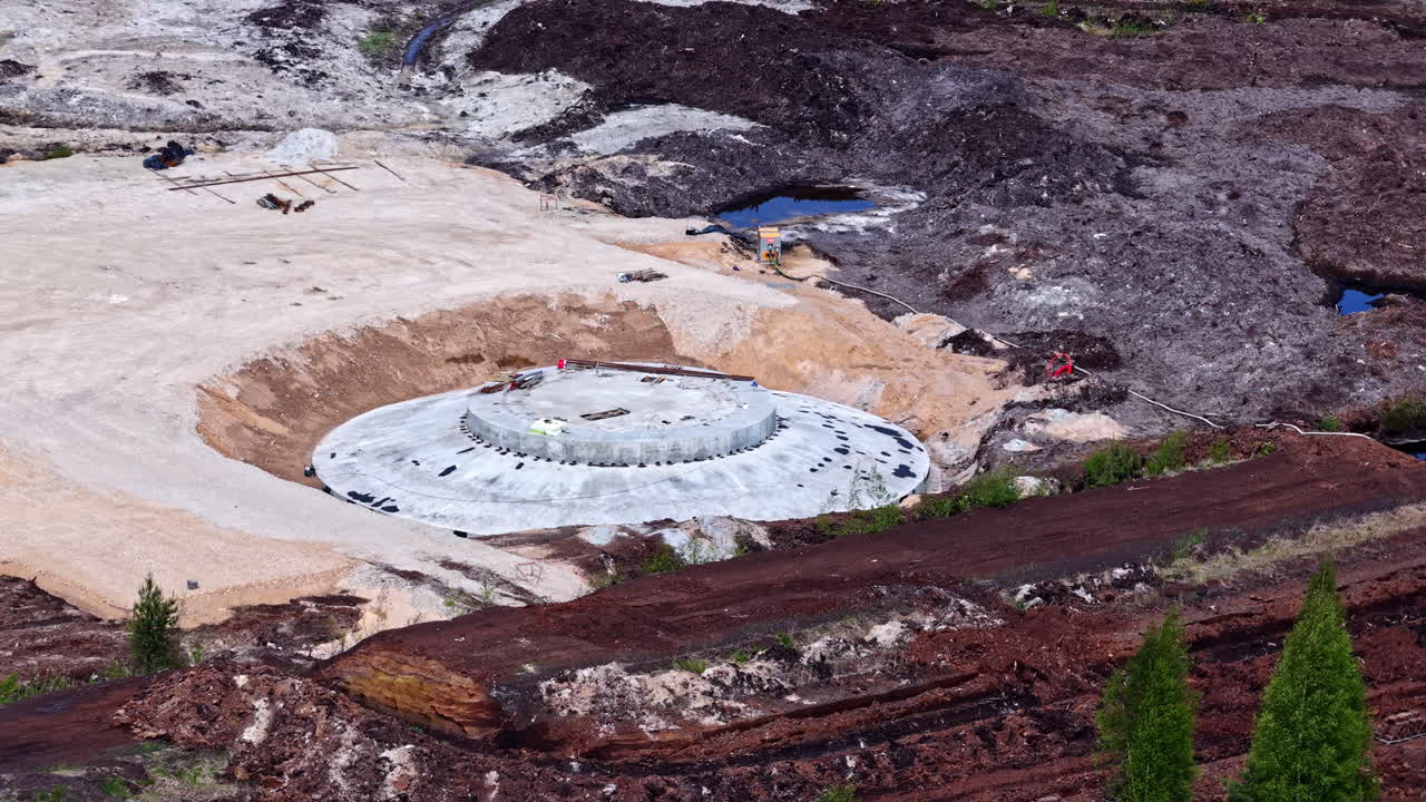 Circular wind turbine foundation under construction surrounded by peat field and equipment