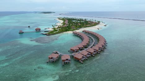 exclusive and noble hotel villas surrounded by blue clear ocean water. maldives island with luxury water villa bungalows. aerial backwards wide shot.
