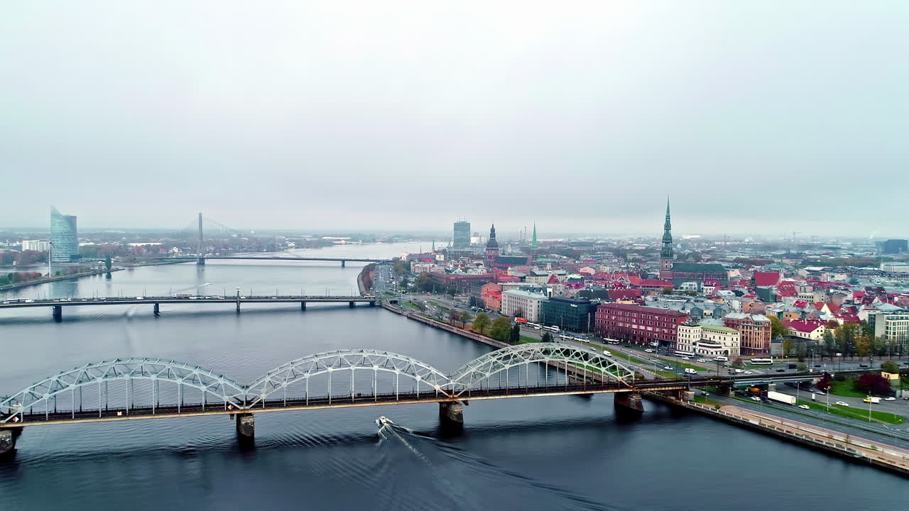 toma aérea de drones volando sobre los puentes sobre el río daugava con el casco antiguo de riga en el fondo en un día nublado en riga, letonia