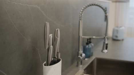 modern kitchen with marble backsplash featuring stainless steel sink, high-end faucet, knife set, and a glimpse of small appliances in the background