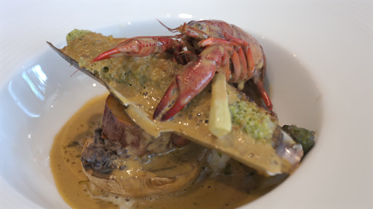Close up of whole cooked crayfish with a mussel shell filled and a creamy herb topping on a white plate