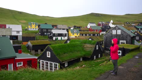 una excursionista disfruta de la vista de la aldea de mykines verdosa con casas coloridas, faroes