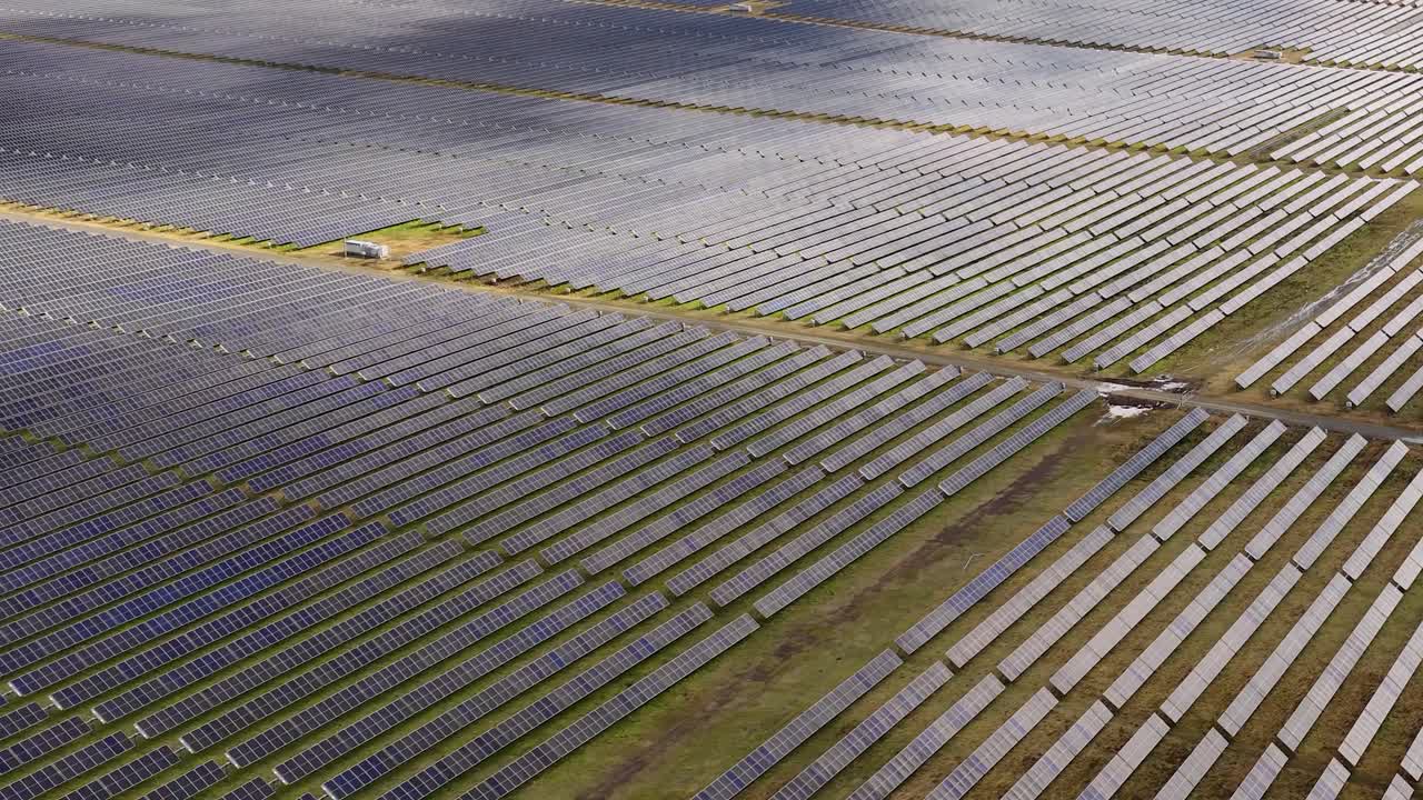 Drone glider hen over et stort solcellepanel under en delvist skyet himmel og indfanger et landskab med vedvarende energi