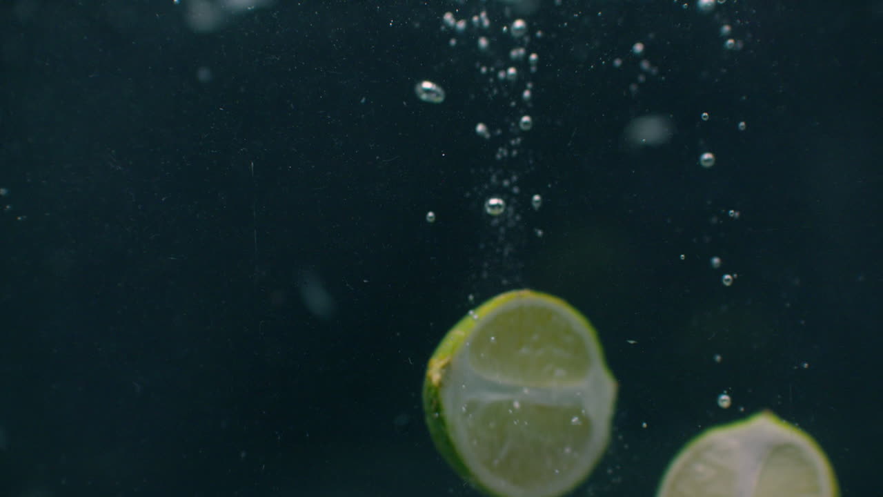 las rebanadas de limón caen y flotan en el agua fondo negro cámara lenta. las rebanas de limón verde caen y flotan en el agua fondo negro cámara lenta