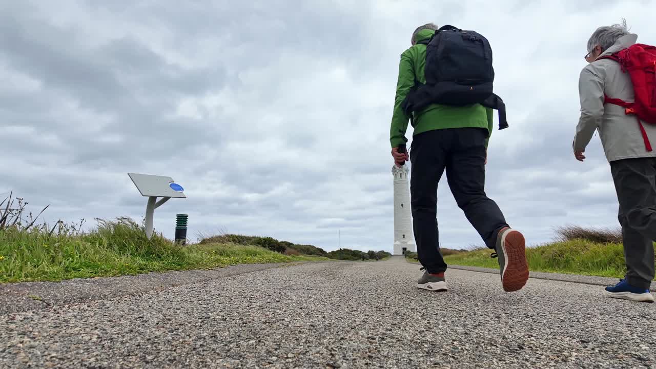 a mature couple in trekking outfits walking past low lying camera along a footpath towards Cape Leeuwin Lighthouse