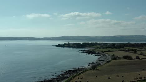 Beautiful-drone-shot-of-green-land-and-seaside-on-summer-afternoon,-dolly-in