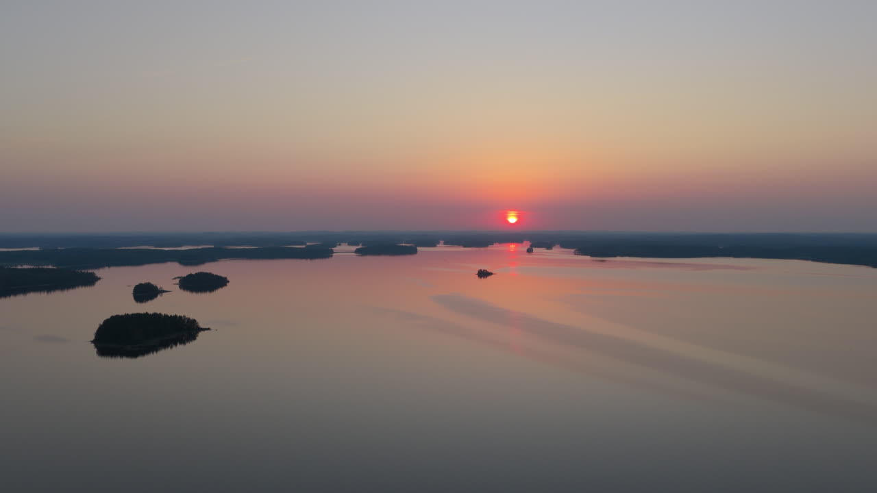 Aerial tracking shot of a red sunset sun above islands on lake Saimaa, Finland