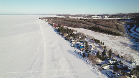 Flying-drone-above-houses-and-a-frozen-lake-during-winter-in-canada