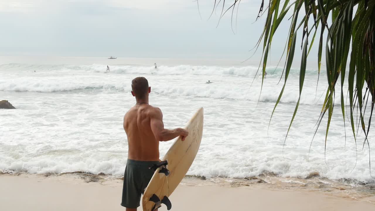 hombre atlético sosteniendo una tabla de surf en una playa tropical de arena en sri lanka
