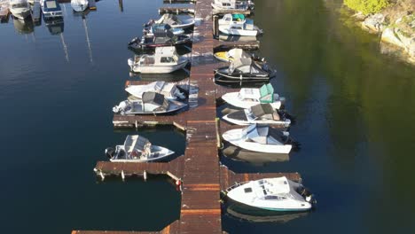 Small-marina-with-multiple-small-boats-moored-at-a-wooden-scaffolding-while-trees-are-reflected-in-the-water