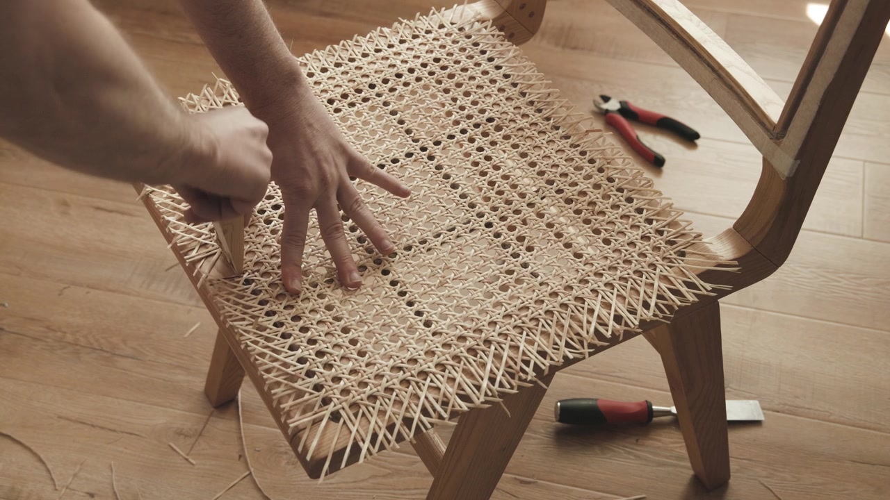 Restauro di una sedia in rattan, un artigiano rimuove le fibre di rattan in eccesso dalla trama.