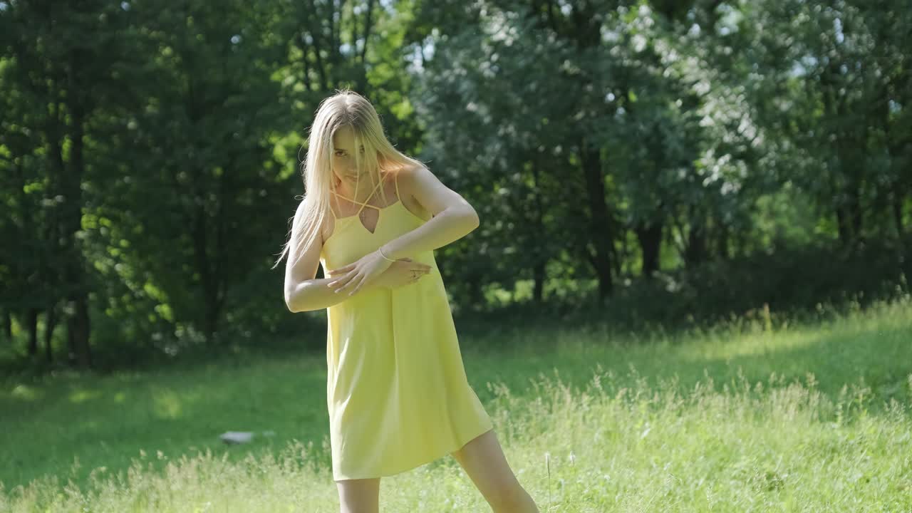 아름다운 젊은 소녀가 자유의 춤을 추고 있습니다. 여름 공원에서 뒷면에 나무가 있습니다.