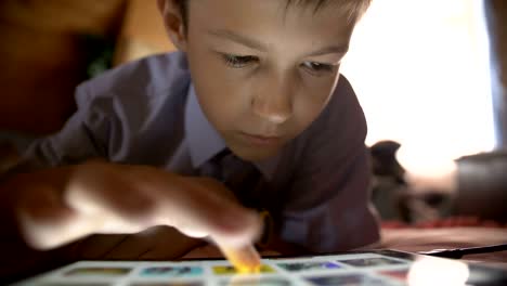 boy lays in a bed and touches on a tablet pc at home