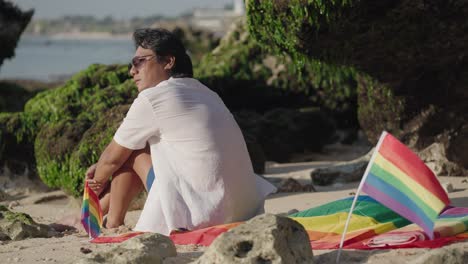 man sitting on beach with pride flag