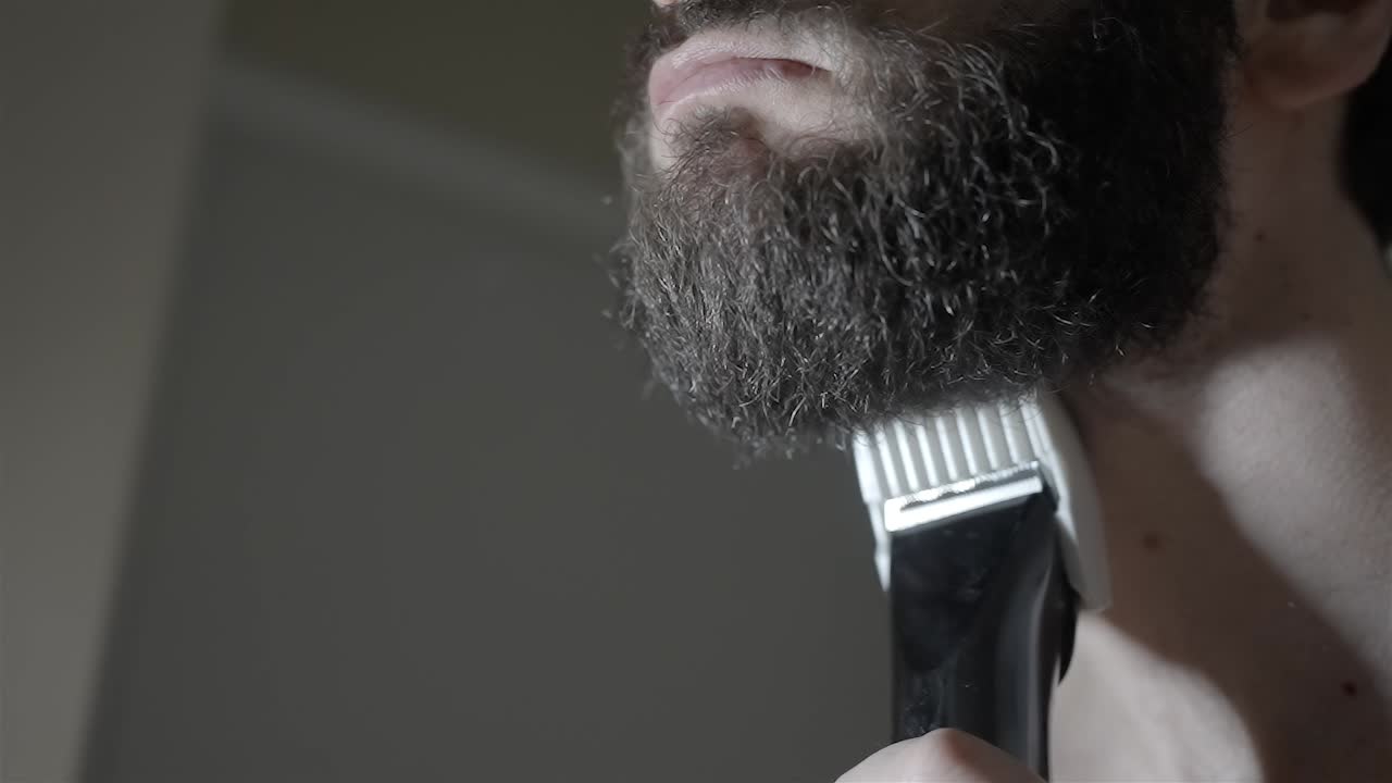 Slow Motion: Man Trimming Thick Beard with Electric Groomer