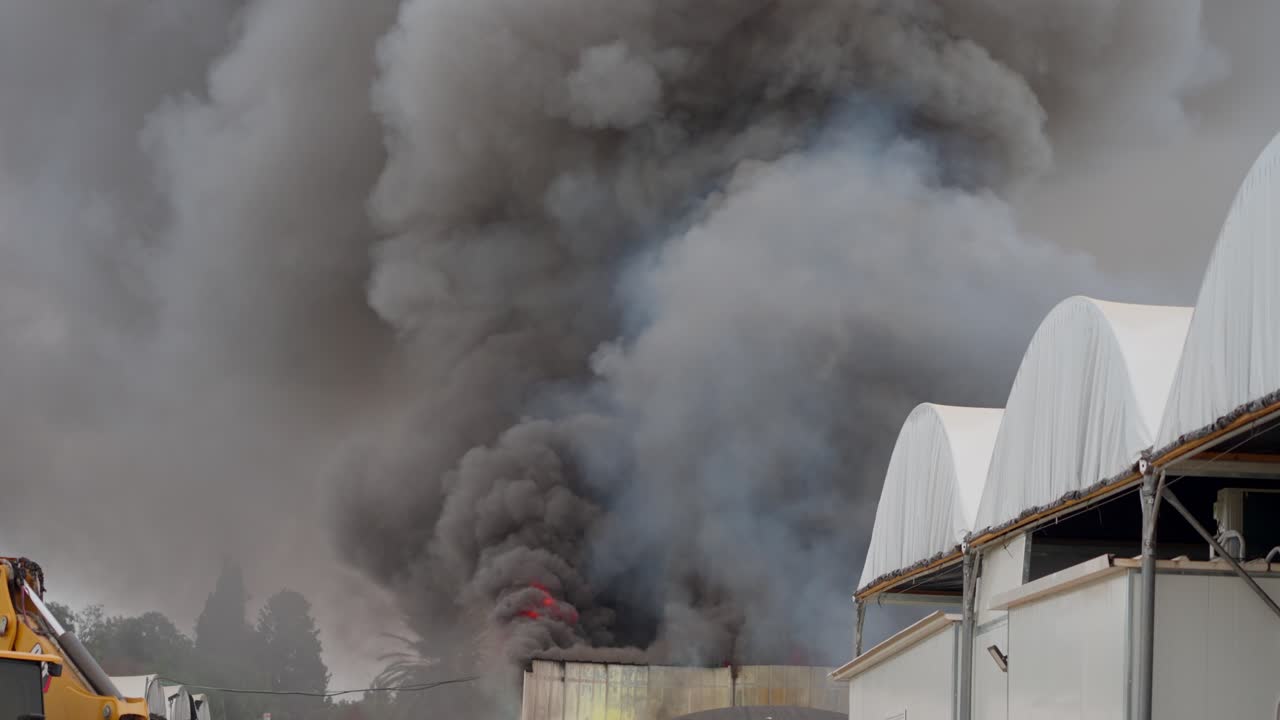 Black smoke clouds and flames rise into the sky from burning warehouses in the village.