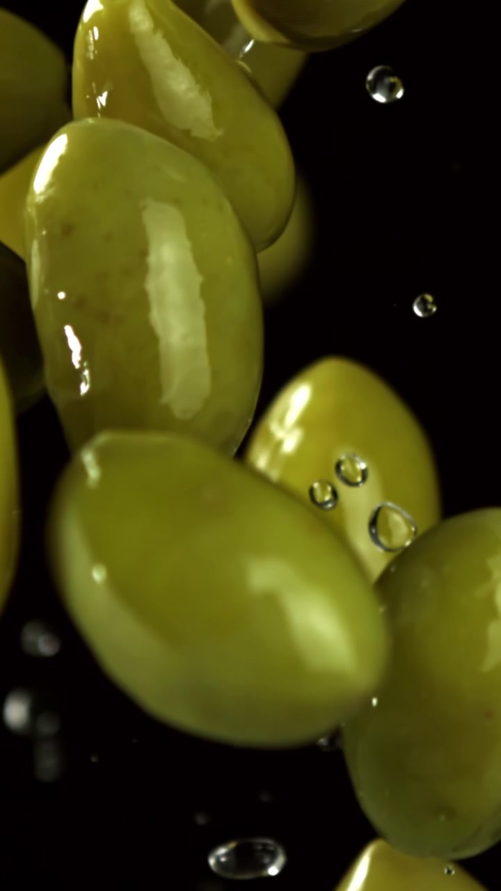 Olive verdi fresche che cadono con gocce d'acqua al rallentatore
