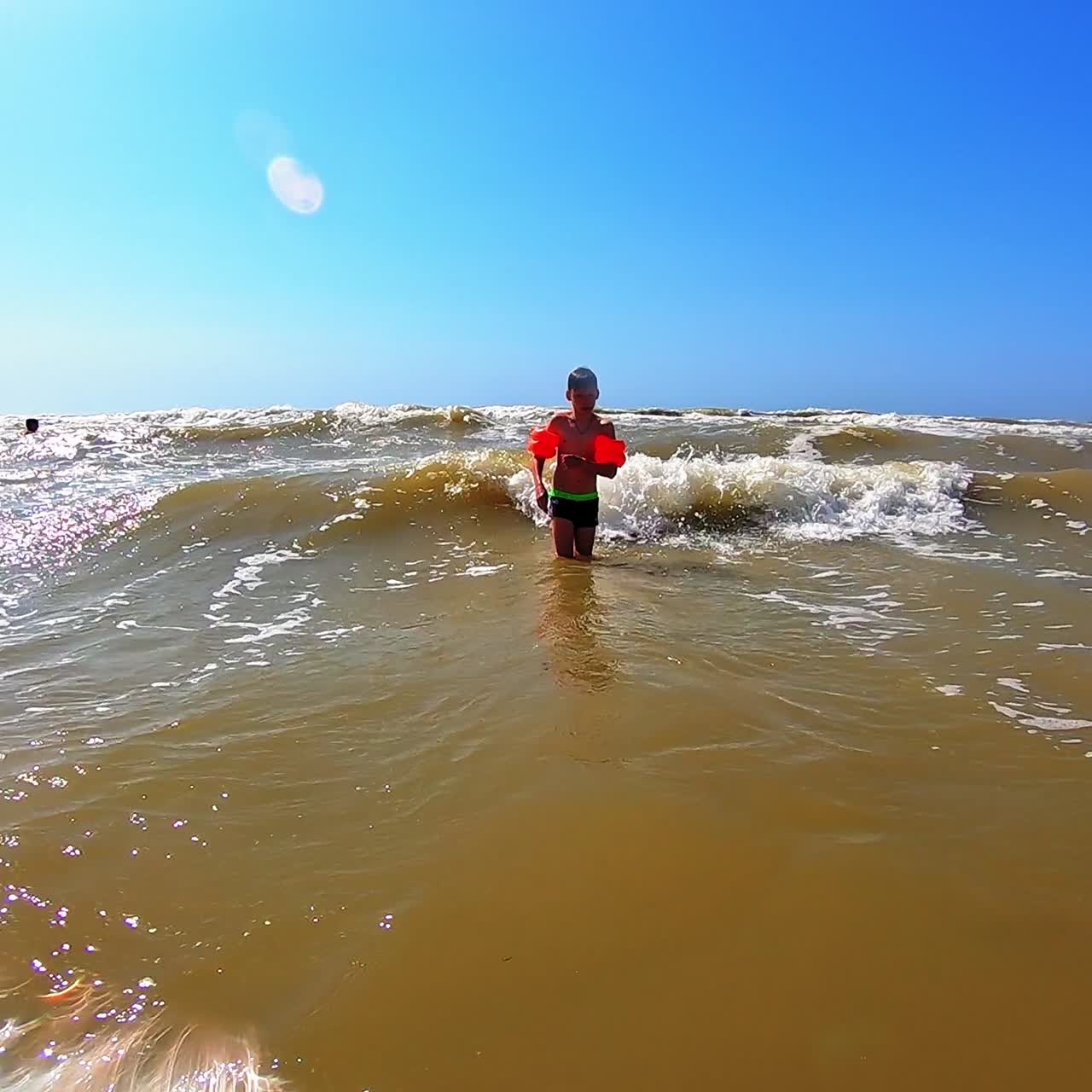 Boy playing in the sea. Bright summer day and small child having fun with foamy waves in the sea water. Slow motion.