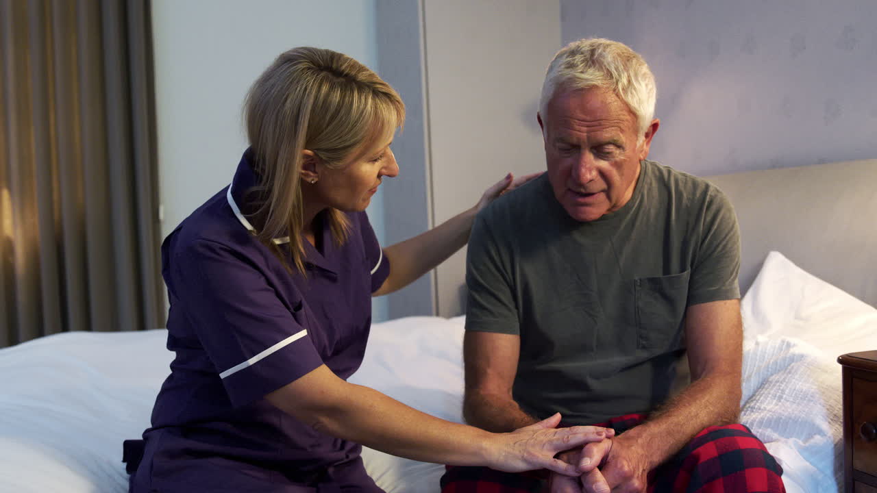 Nurse Talking With Unhappy Senior Man In Bedroom On Home Visit