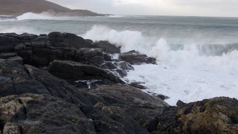 slow motion shot of large breaking waves crashing over the rocks during a storm in the bay by tangasdale beach, near castlebay on the isle of barra