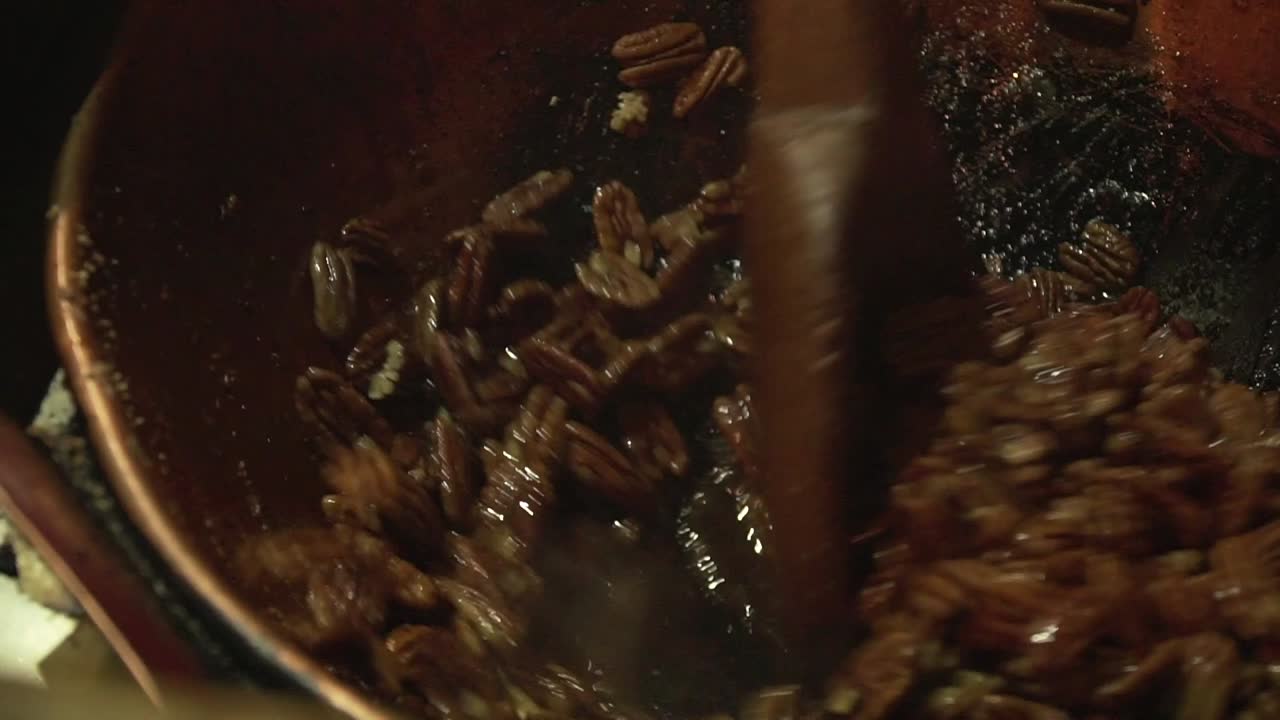 Ripresa ravvicinata al rallentatore di noci pecan tostate e caramellate che vengono mescolate con una grande spatola di legno.