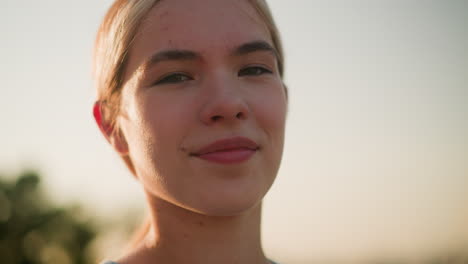 close-up of young lady smiling under warm sunlight, with eyes closed, capturing her natural expression and sense of happiness, soft bokeh effect from greenery in background